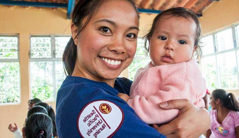 A nursing student holding a baby on a study abroad trip